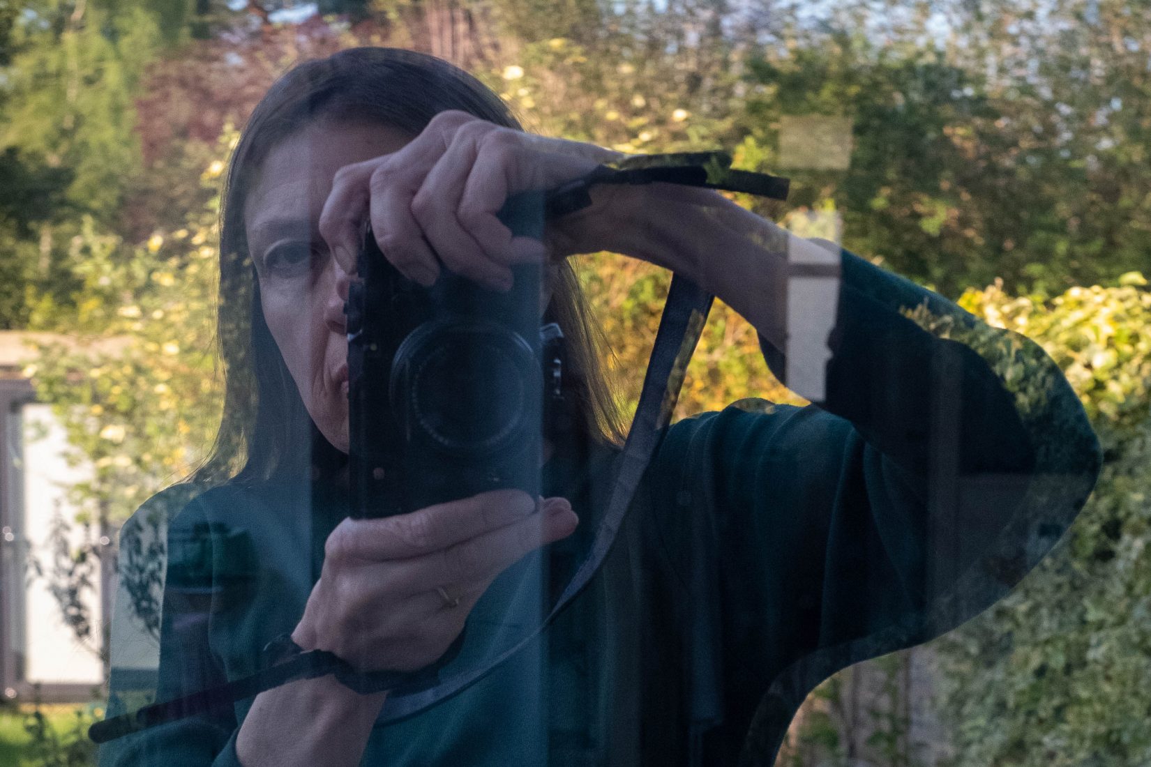 Karren, a photographer, holds the camera in front of her face to take a self portrait using the reflection of a window, when experimenting in lockdown April 2020